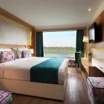 An elegant, wood-paneled hotel room on the MS Acamar Nile Cruise ship features twin beds, panoramic windows overlooking the Nile River, and modern furnishings.