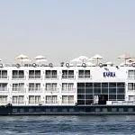 The magnificent Al Kahila Nile cruise ship sailing smoothly on the river with its multi-deck structure and sun loungers on top.