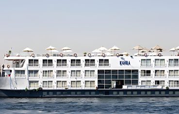 The magnificent Al Kahila Nile cruise ship sailing smoothly on the river with its multi-deck structure and sun loungers on top.
