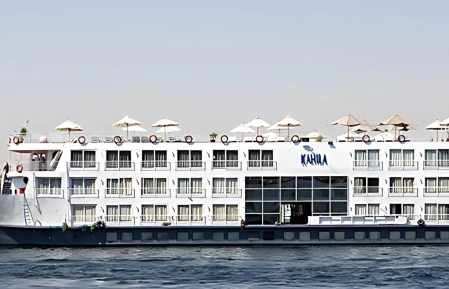The magnificent Al Kahila Nile cruise ship sailing smoothly on the river with its multi-deck structure and sun loungers on top.