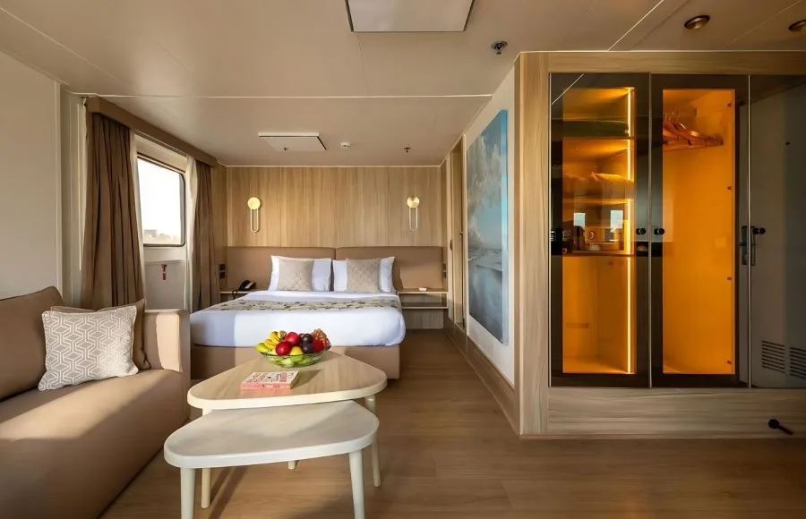 An interior photo of a suite on the MS Alexander The Great Nile cruise ship, showing the bed, couch, and window view.