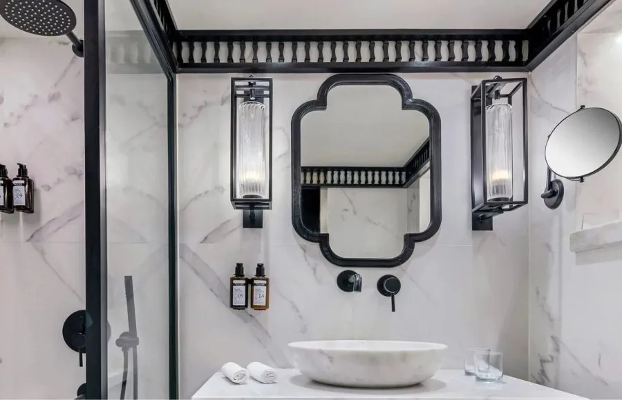 The luxurious bathroom in the suite aboard the Movenpick MS Darakum Nile Cruise features elegant marble tiling a modern rain shower and a stylish black-framed mirror