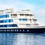 The striking exterior of the multi-decked Movenpick MS Darakum Nile Cruise sailing on the blue river with its many windows and top-deck sun umbrellas clearly visible
