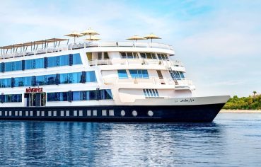 The striking exterior of the multi-decked Movenpick MS Darakum Nile Cruise sailing on the blue river with its many windows and top-deck sun umbrellas clearly visible