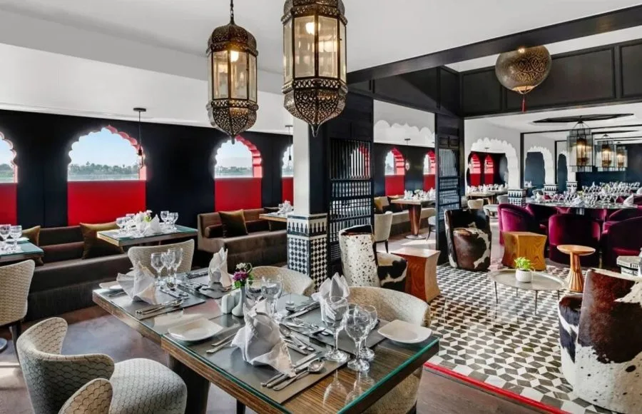 The exquisitely designed main restaurant on the Movenpick MS Darakum Nile Cruise offers elegant table settings ornate Moroccan lamps and arched windows with Nile views