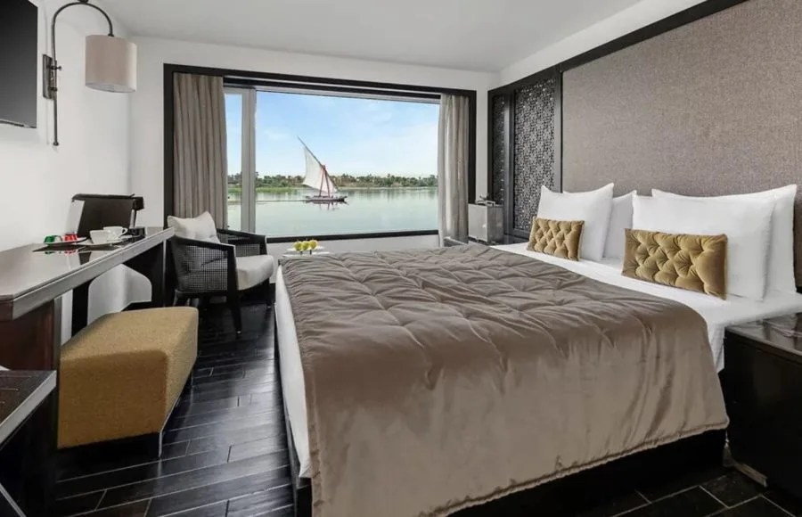 Luxurious suite aboard the Movenpick MS Darakum Nile Cruise offering a stunning Nile panorama with a traditional sailboat passing by for an unforgettable journey