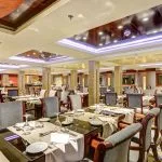 Elegant cruise ship dining room with set tables and decorative lighting.
