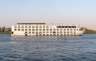 The MS Jaz Regent Nile Cruise ship sailing on the Nile River, with its multi-deck structure visible against the riverbanks.