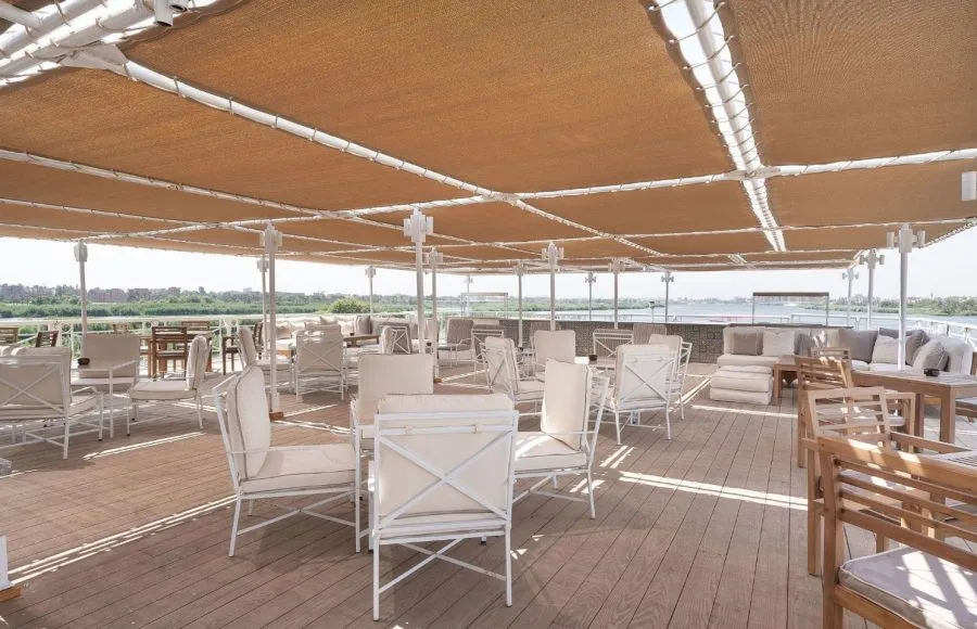 The sun deck of the MS Jaz Regent Nile Cruise, featuring a small pool, numerous lounge chairs with umbrellas, and a view of the Nile River banks.