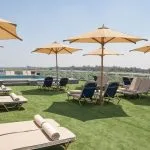 The expansive sun deck of the MS Jaz Regent Nile Cruise, featuring a small pool, numerous lounge chairs with umbrellas, and a view of the Nile River banks.