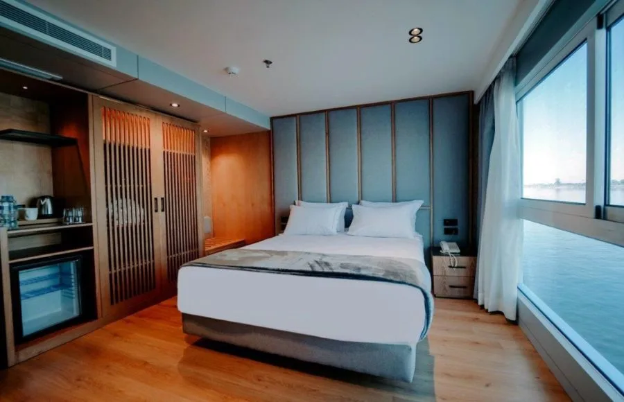 A comfortable and modern cabin on the MS Miriam Nile Cruise featuring a cozy bed and large window with a river view