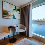 Enjoy the stunning Nile river view from a comfortable MS Miriam Nile Cruise cabin with stylish seating and modern decor