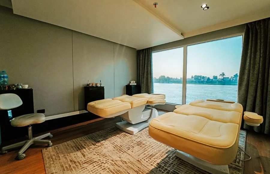 A tranquil massage room with treatment tables and a panoramic window view of the Nile river on the MS Miriam nile cruise ship