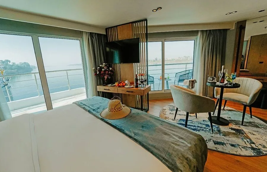 A luxurious standard cabin on the MS Miriam Nile Cruise featuring a comfortable bed, sitting area, and private balcony overlooking the water