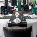 Elegant dining setup inside the Movenpick Hamees Nile Cruise restaurant featuring crisp white linens, deep green accents, and a red rose centerpiece awaiting guests.