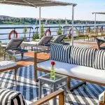 Panoramic view from the sundeck of the Movenpick Hamees Nile Cruise, featuring comfortable loungers and stunning river scenery with traditional sailboats.