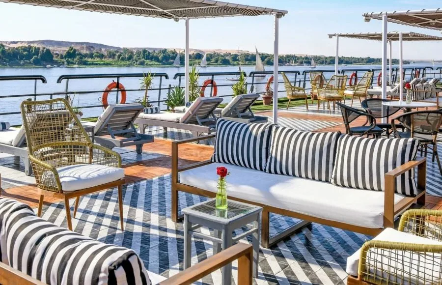 Panoramic view from the sundeck of the Movenpick Hamees Nile Cruise, featuring comfortable loungers and stunning river scenery with traditional sailboats.
