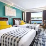 A twin-bed cabin on the Movenpick MS Sunray featuring colorful decor and a large window overlooking the Nile River.