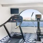 The fitness center on the Movenpick MS Sunray featuring cardio equipment with a scenic view of the Nile River.