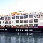 Exterior view of the white and black Movenpick MS Sunray boat sailing on the Nile River under a clear sky.