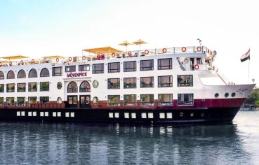 Exterior view of the white and black Movenpick MS Sunray boat sailing on the Nile River under a clear sky.