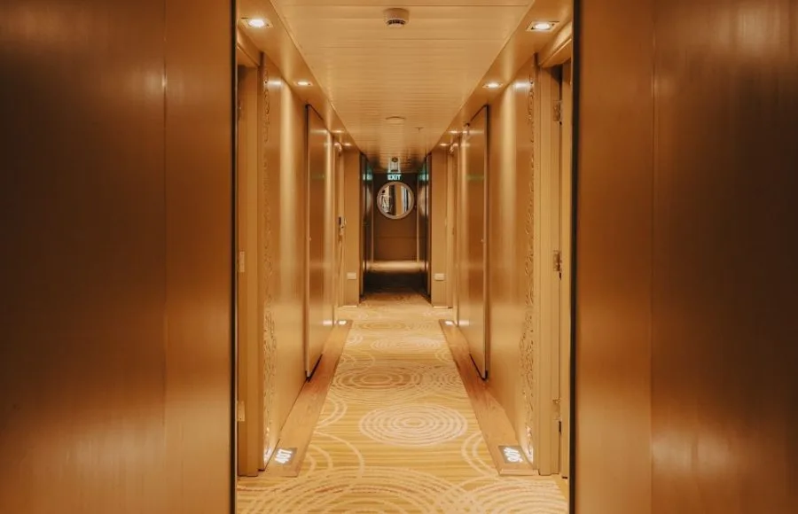 Ship corridor with tan walls, patterned carpet, and recessed lighting.