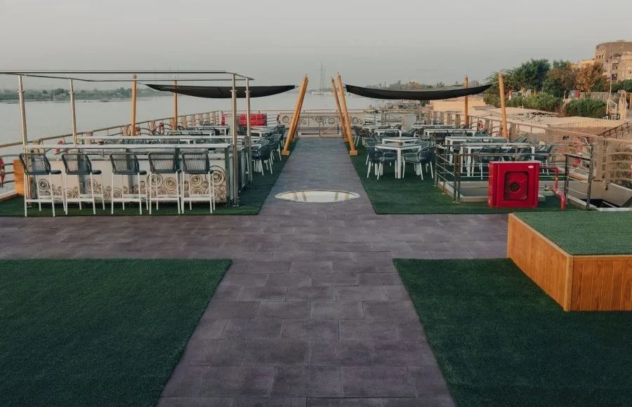 Wide view of a ship's sundeck with a bar and dining tables.