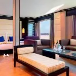 Spacious, luxurious suite on the Ms Nile Premium cruise ship featuring a separate seating area, plush bed, and panoramic windows with a river view.