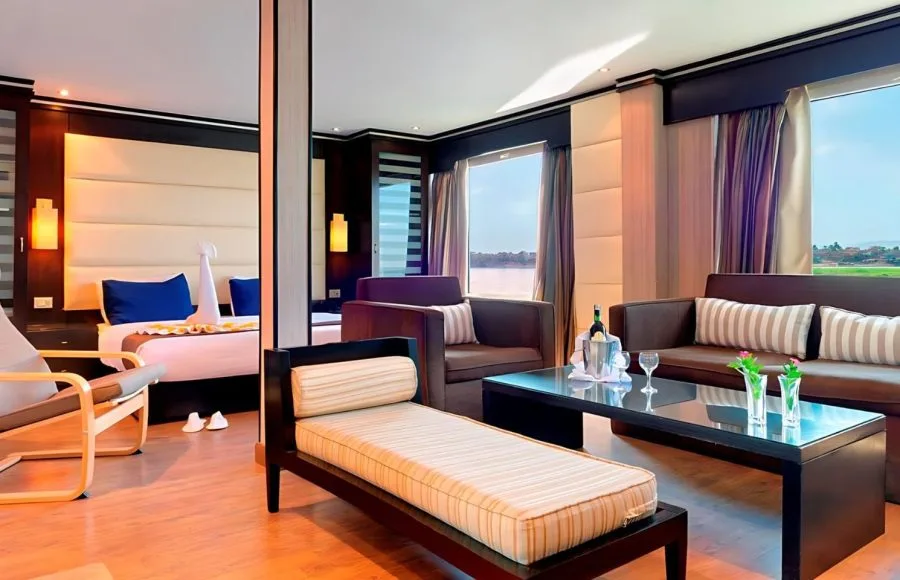 Spacious, luxurious suite on the Ms Nile Premium cruise ship featuring a separate seating area, plush bed, and panoramic windows with a river view.