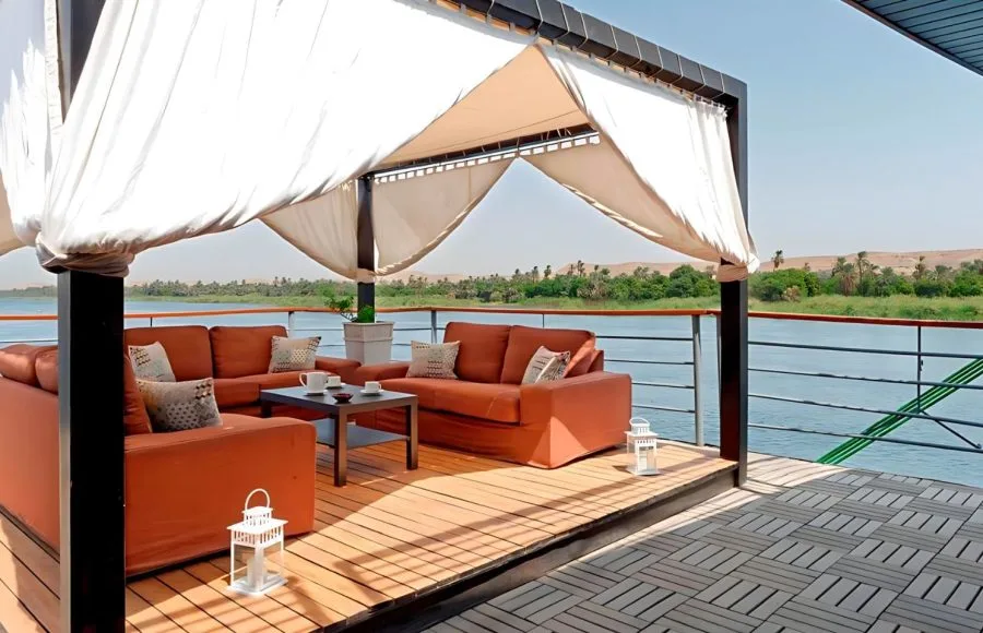 A shaded outdoor seating area with comfortable sofas and stunning river views on the sundeck of the ms nile premium cruise.