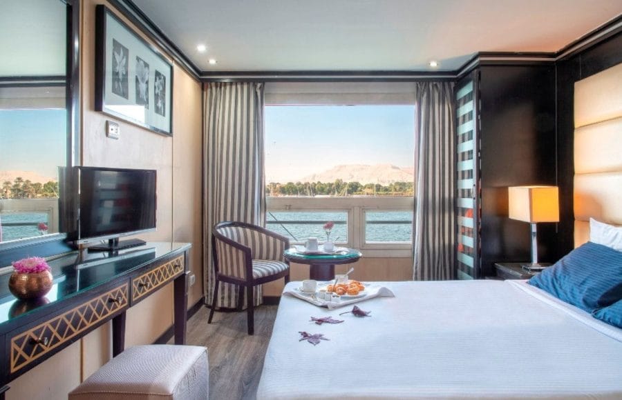 Deluxe suite on the MS Nile Style Cruise Ship with a queen bed and a picturesque view of the Nile River.