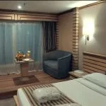 A comfortable cabin on the Princess Sarah I Nile Cruise with a single bed, a cozy chair, and a Nile view.