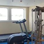 Small cruise ship gym with large windows overlooking the Nile, a treadmill, and a multi-station weight machine.