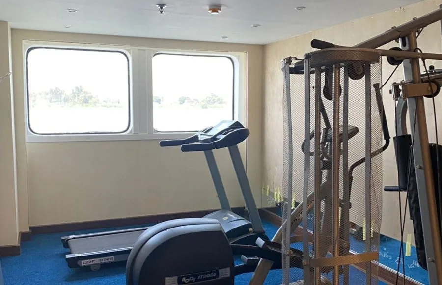 Small cruise ship gym with large windows overlooking the Nile, a treadmill, and a multi-station weight machine.