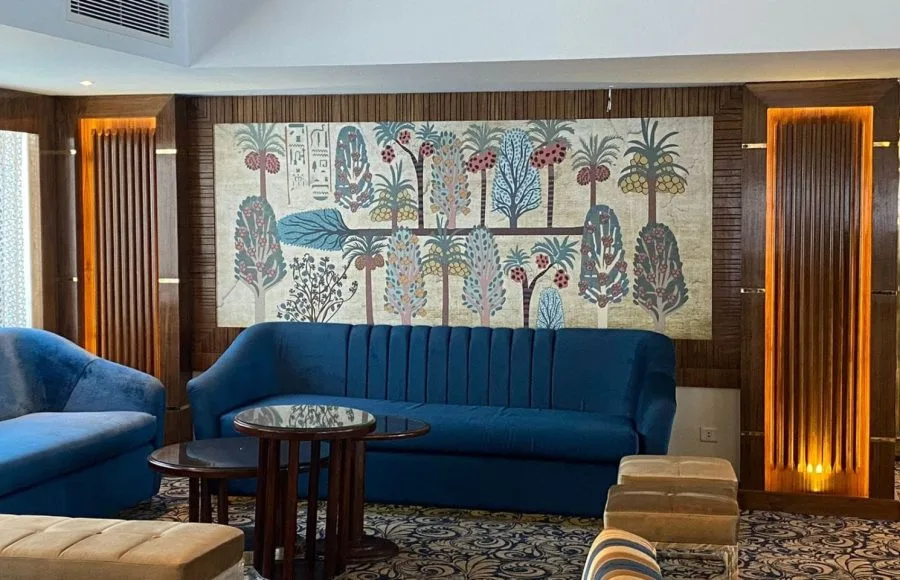 Blue velvet sofa in a cruise lobby with a large tapestry depicting trees and hieroglyphs.