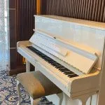 White upright piano with a subtle speckled design and a fabric bench, set on a blue patterned carpet.
