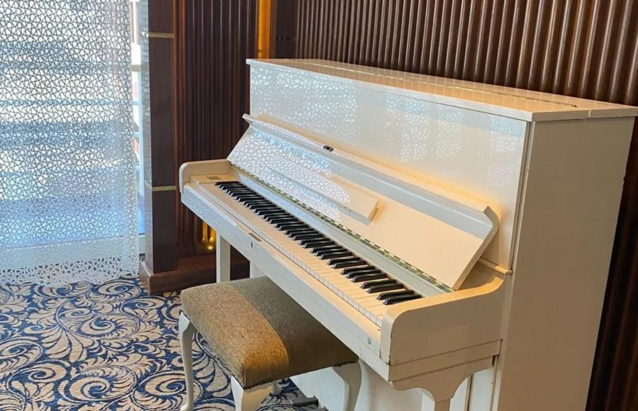 White upright piano with a subtle speckled design and a fabric bench, set on a blue patterned carpet.