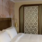 Cruise cabin wardrobe doors with white Art Deco lattice screens next to a bed with Art Deco fan pattern wallpaper.