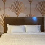 Double bed in a cruise cabin with a dark wood headboard, brass wall lamps, and Art Deco-style fan pattern wallpaper.