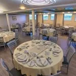 Formal dining room with multiple round tables set with white linens and elegant place settings.