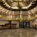 Grand, multi-story atrium/lobby with a marble floor, ornate railings, and a large, stained-glass dome ceiling.