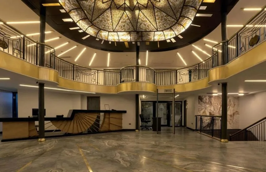 Grand, multi-story atrium/lobby with a marble floor, ornate railings, and a large, stained-glass dome ceiling.