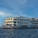 A white, multi-deck cruise ship, "Nile Goddess," sailing on the water under a clear blue sky.