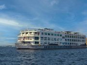 A White, Multi-Deck Cruise Ship, &Quot;Nile Goddess,&Quot; Sailing On The Water Under A Clear Blue Sky.