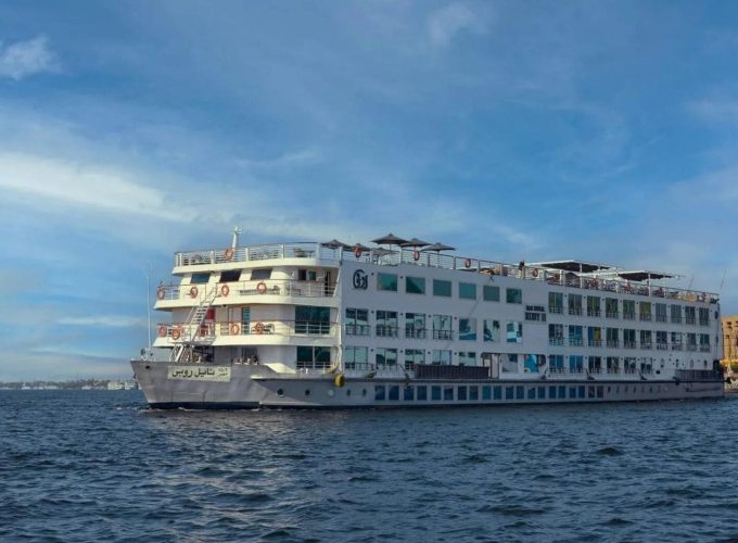 A White, Multi-Deck Cruise Ship, &Quot;Nile Goddess,&Quot; Sailing On The Water Under A Clear Blue Sky.