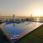 Rooftop pool area at sunset with lounge chairs, featuring a uniquely shaped pool overlooking the river.