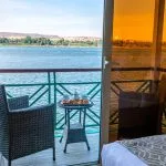 A private balcony on the Sonesta Moon Goddess Nile Cruise ship, set with a small table and chairs, offering a serene view of the Nile River.