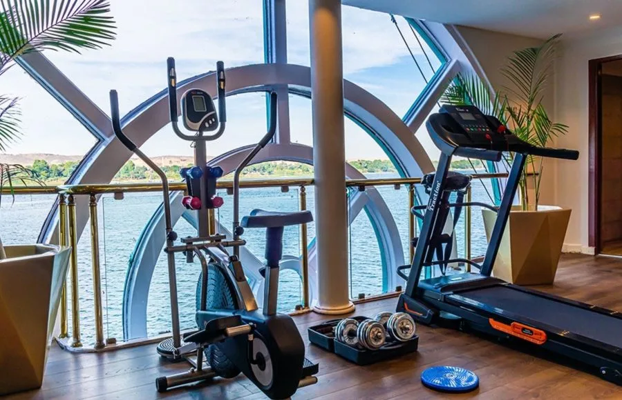The modern fitness center on the Sonesta Moon Goddess Nile Cruise ship, equipped with various exercise machines and panoramic windows overlooking the Nile.