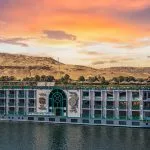 The impressive Sonesta Moon Goddess Nile Cruise ship sails along the river, its striking design highlighted by the beautiful desert landscape at sunset.