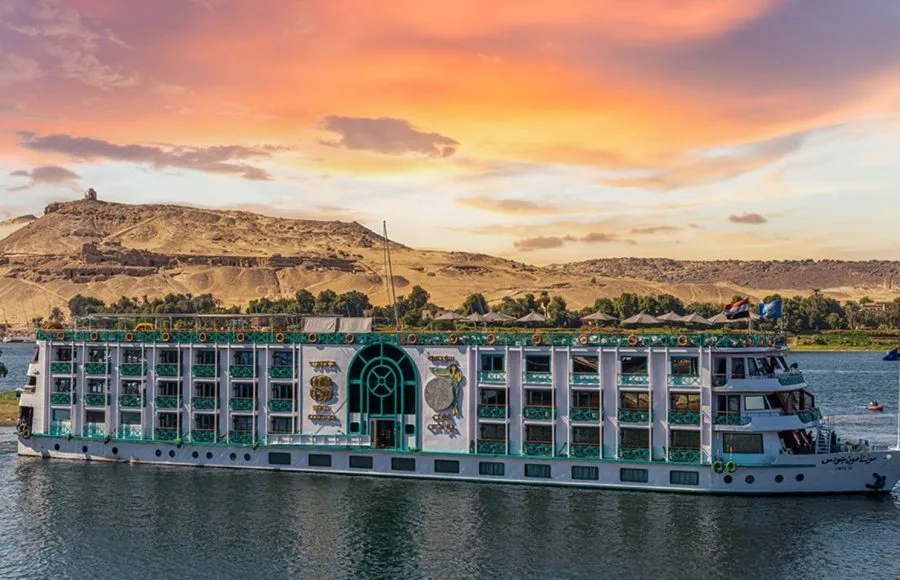 The impressive Sonesta Moon Goddess Nile Cruise ship sails along the river, its striking design highlighted by the beautiful desert landscape at sunset.